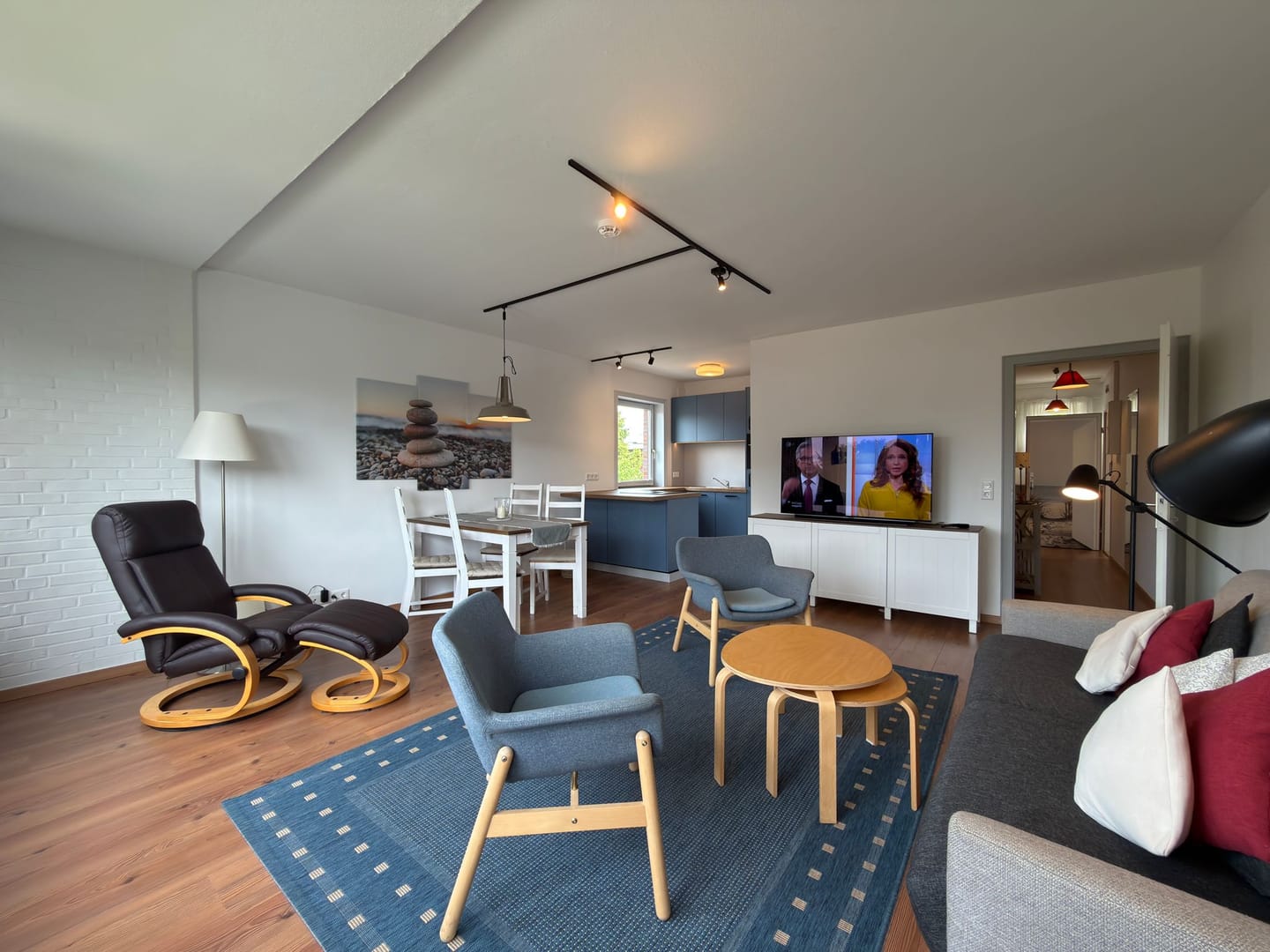 Offener Wohn- und Essbereich mit Relaxsessel, Esstisch und Kieselstrand-Wandbild